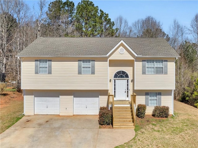 split foyer home with a front yard, concrete driveway, an attached garage, and a shingled roof