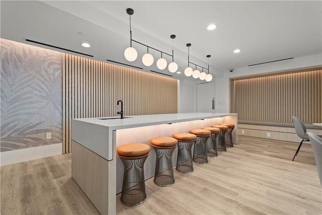 bar featuring light wood-type flooring, indoor wet bar, a sink, and decorative light fixtures