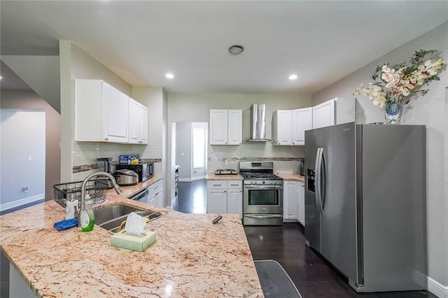 kitchen featuring wall chimney range hood, appliances with stainless steel finishes, tasteful backsplash, a sink, and a peninsula