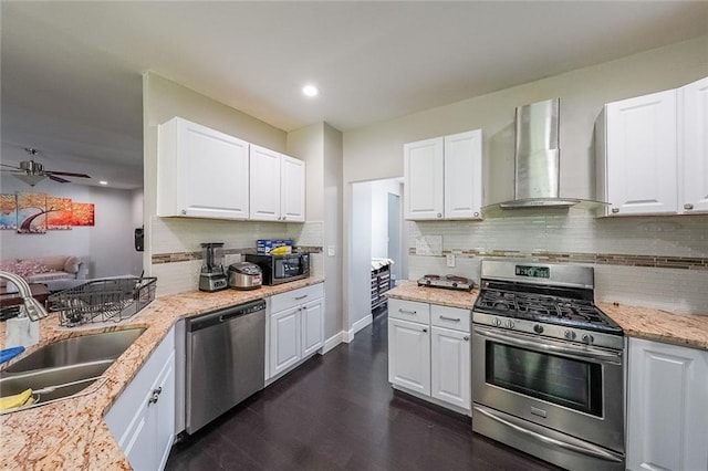 kitchen with ceiling fan, wall chimney exhaust hood, white cabinetry, a sink, and appliances with stainless steel finishes