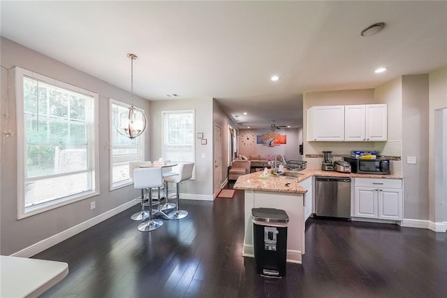 kitchen with a sink, dark wood finished floors, a peninsula, white cabinetry, and stainless steel dishwasher