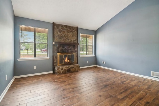 unfurnished living room featuring dark hardwood / wood-style floors, lofted ceiling, and a stone fireplace