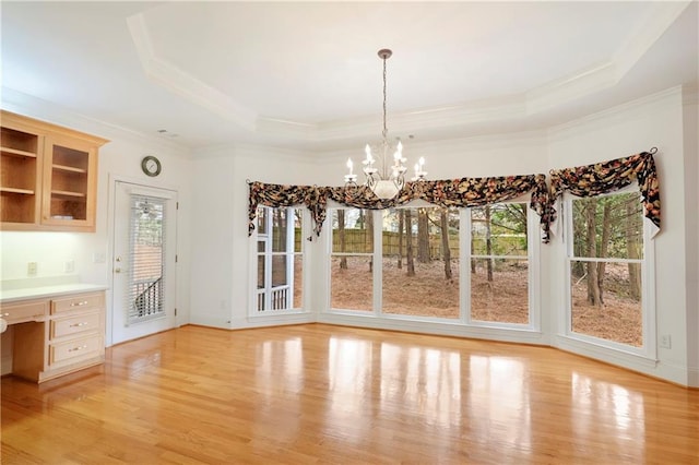 unfurnished dining area featuring built in desk, a chandelier, light wood-type flooring, and a raised ceiling