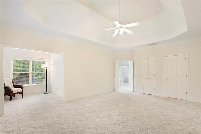 spare room featuring a raised ceiling, crown molding, light colored carpet, and ceiling fan