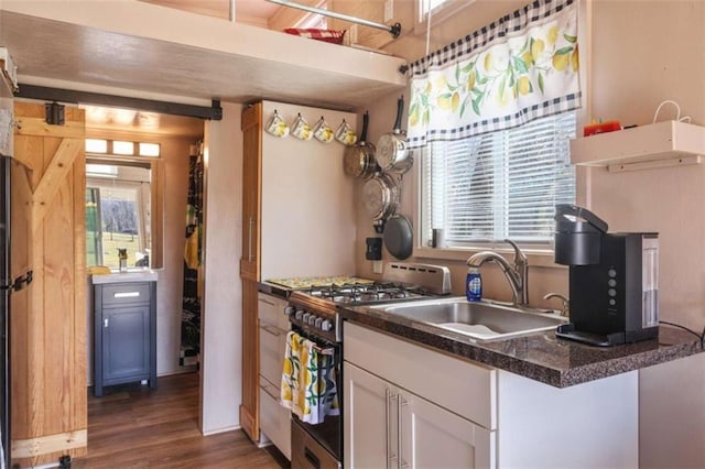 kitchen with dark wood-style floors, gas stove, white cabinets, a sink, and dark stone countertops