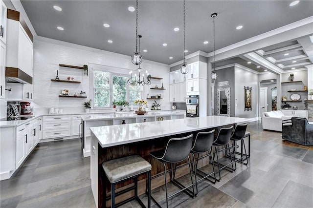 kitchen with white cabinetry, decorative light fixtures, a spacious island, black electric cooktop, and a breakfast bar area