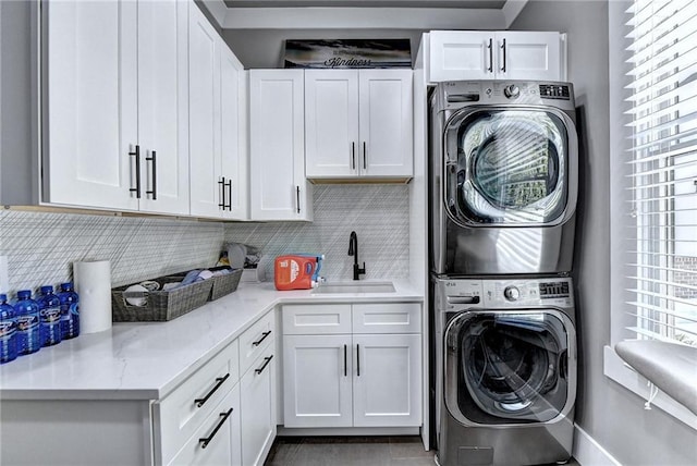 laundry area featuring stacked washing maching and dryer, sink, and cabinets