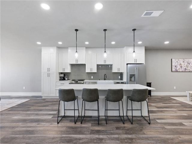 kitchen featuring white cabinets, hanging light fixtures, stainless steel refrigerator with ice dispenser, and a kitchen island with sink