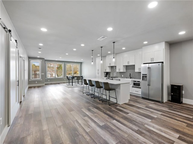 kitchen featuring white cabinetry, a kitchen island with sink, decorative light fixtures, a barn door, and stainless steel fridge