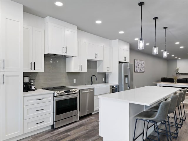 kitchen featuring appliances with stainless steel finishes, decorative light fixtures, a kitchen island, sink, and white cabinetry