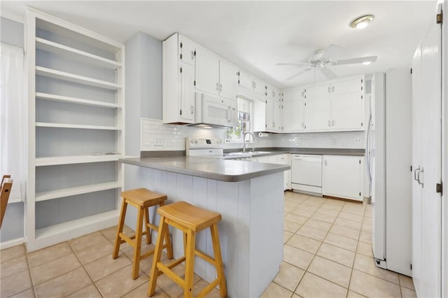 kitchen with light tile patterned floors, a peninsula, white appliances, a sink, and a ceiling fan