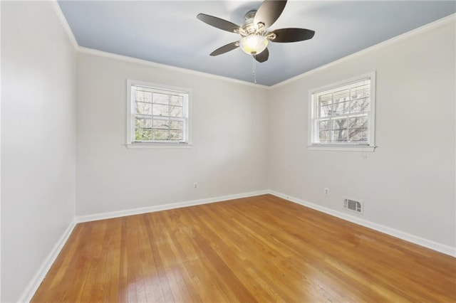 empty room with light wood finished floors, ornamental molding, a wealth of natural light, and visible vents