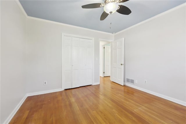 unfurnished bedroom with a closet, visible vents, ornamental molding, wood finished floors, and baseboards