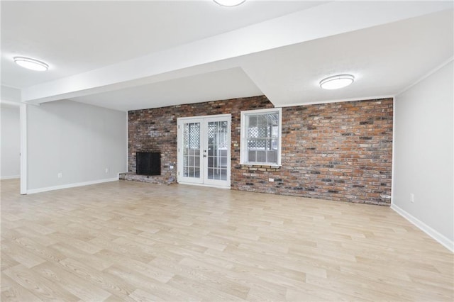 unfurnished living room with brick wall, a fireplace, baseboards, light wood-style floors, and french doors