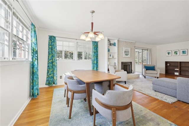 dining area featuring a brick fireplace, baseboards, light wood finished floors, and a notable chandelier