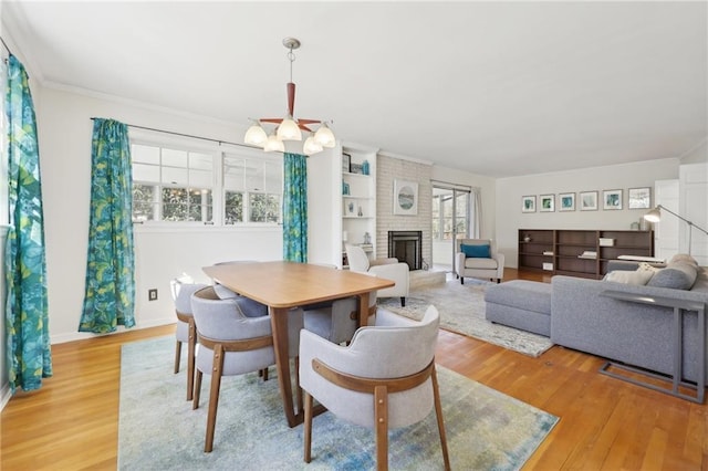 dining area with a chandelier, light wood finished floors, a fireplace, and ornamental molding