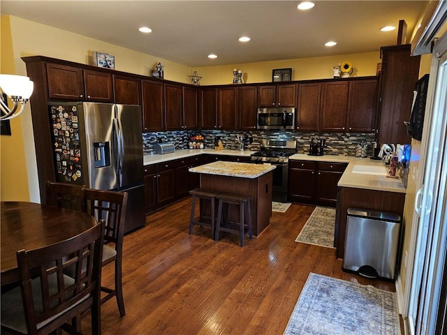 kitchen with a breakfast bar area, appliances with stainless steel finishes, dark brown cabinets, a center island, and dark hardwood / wood-style flooring