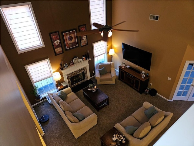 living room featuring a tile fireplace, carpet floors, ceiling fan, and a towering ceiling