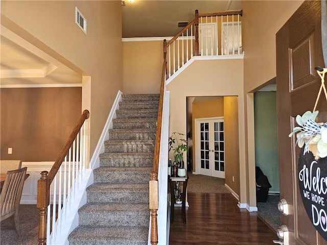 stairs featuring french doors, a towering ceiling, ornamental molding, and hardwood / wood-style floors