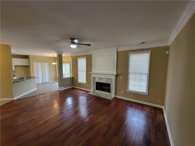 unfurnished living room with dark wood-style flooring, a ceiling fan, baseboards, a high end fireplace, and crown molding