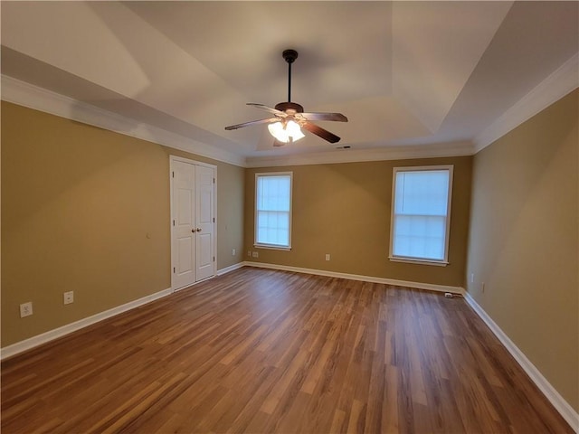 spare room featuring a tray ceiling, crown molding, wood finished floors, ceiling fan, and baseboards