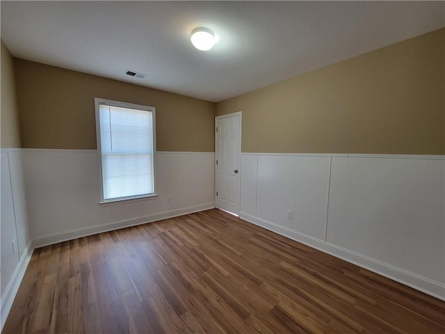 empty room featuring wood finished floors and wainscoting