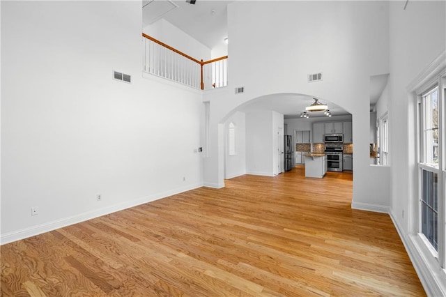 4120 Lakeside Blvd, Monroe, GA 30655 - unfurnished living room featuring arched walkways, light wood-type flooring, a towering ceiling, and baseboards
