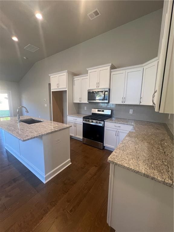 kitchen with sink, appliances with stainless steel finishes, light stone countertops, an island with sink, and white cabinets