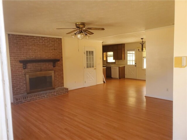 unfurnished living room with light wood finished floors, a brick fireplace, a ceiling fan, and crown molding