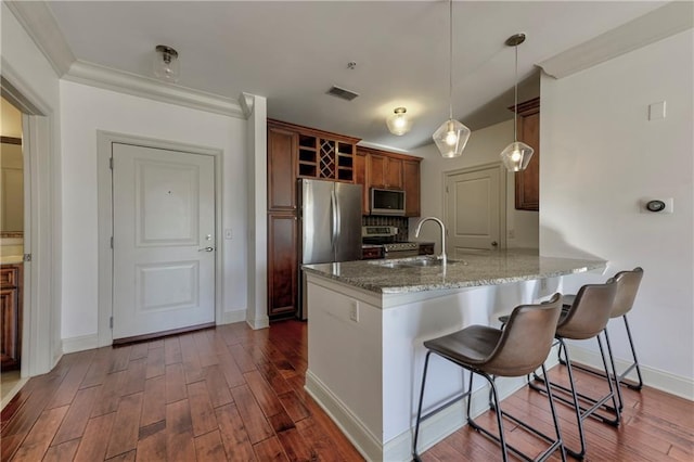 kitchen with sink, a breakfast bar, appliances with stainless steel finishes, hanging light fixtures, and light stone counters