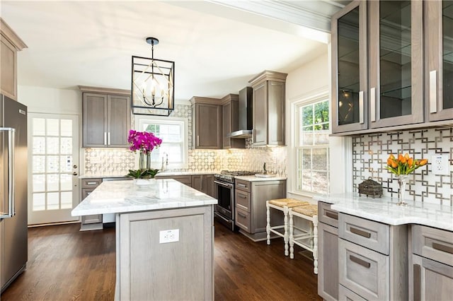 kitchen with a center island, pendant lighting, appliances with stainless steel finishes, wall chimney range hood, and light stone countertops