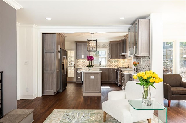 kitchen with a center island, pendant lighting, stainless steel appliances, light countertops, and glass insert cabinets