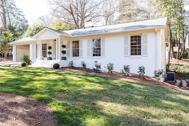 ranch-style home featuring a chimney, covered porch, cooling unit, a front lawn, and brick siding