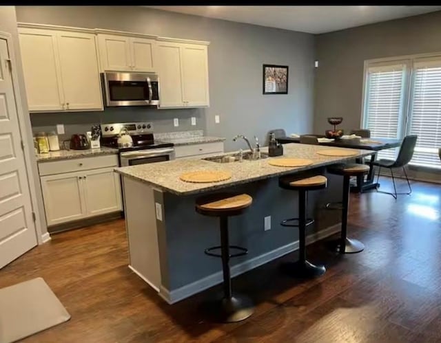 11547 Hathaway Dr, Hampton, GA 30228 - kitchen featuring appliances with stainless steel finishes, dark wood-style floors, white cabinets, an island with sink, and a kitchen bar