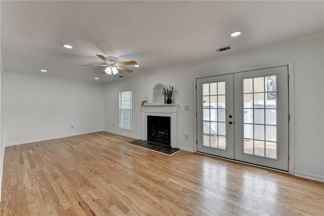 unfurnished living room featuring french doors, crown molding, light hardwood / wood-style flooring, ceiling fan, and a fireplace