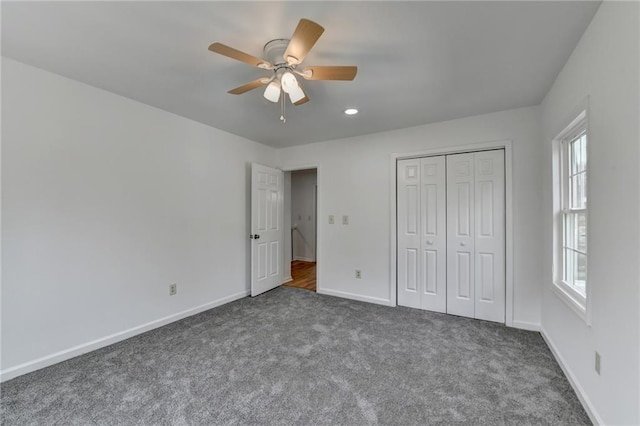 unfurnished bedroom with multiple windows, dark colored carpet, ceiling fan, and a closet