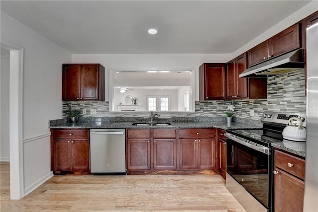 kitchen with sink, appliances with stainless steel finishes, tasteful backsplash, dark stone counters, and light wood-type flooring