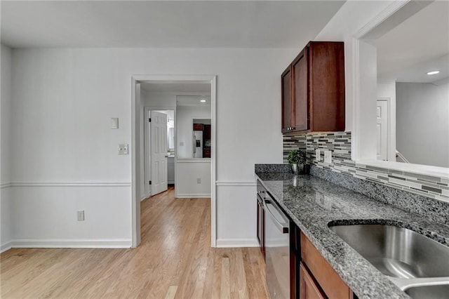 kitchen featuring sink, dishwasher, tasteful backsplash, dark stone counters, and light wood-type flooring