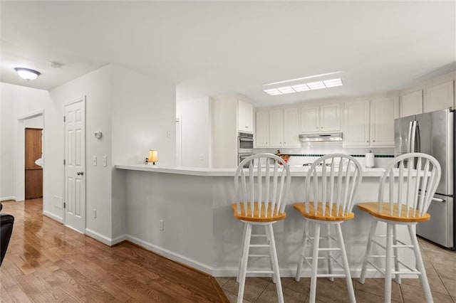1418 Mill Path Loop, Lawrenceville, GA 30045 - kitchen with stainless steel appliances, under cabinet range hood, light wood finished floors, and a kitchen bar