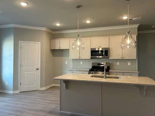 kitchen with light stone counters, white cabinets, decorative light fixtures, and appliances with stainless steel finishes