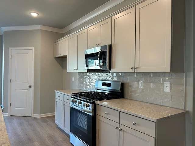 kitchen featuring light stone countertops, stainless steel appliances, ornamental molding, backsplash, and light wood-type flooring