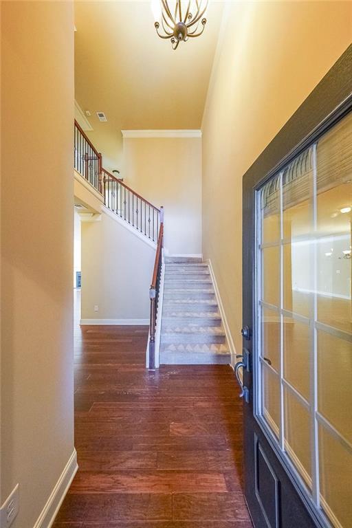 stairway with hardwood / wood-style flooring, ornamental molding, and an inviting chandelier