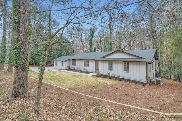 view of front of home with board and batten siding, a shingled roof, central AC, and a front yard