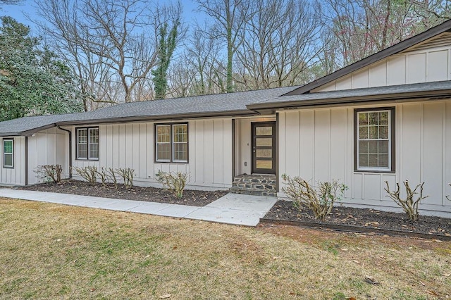 entrance to property with a yard, a shingled roof, and board and batten siding