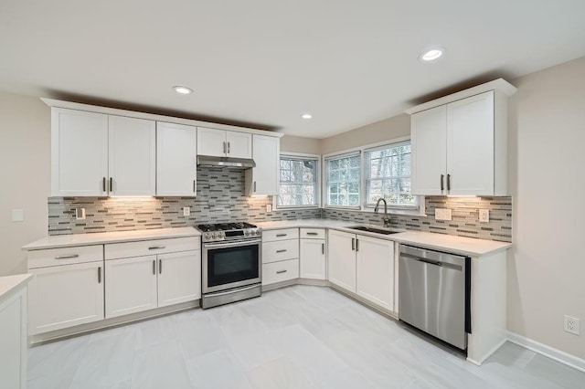 kitchen with stainless steel appliances, light countertops, white cabinets, a sink, and under cabinet range hood