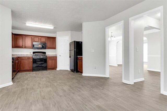 2146 Silva Ct, Conley, GA 30288 - kitchen featuring black appliances, arched walkways, light wood-style flooring, baseboards, and a textured ceiling