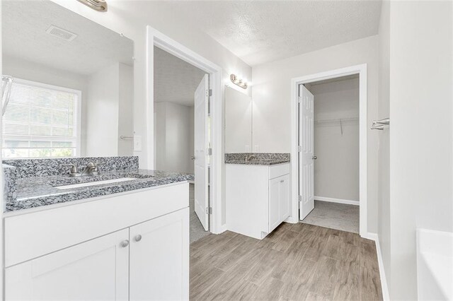 2146 Silva Ct, Conley, GA 30288 - full bathroom featuring wood finished floors, two vanities, a walk in closet, a textured ceiling, and baseboards