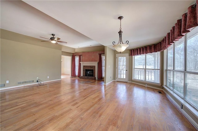 unfurnished living room featuring ceiling fan, a healthy amount of sunlight, a fireplace, and light hardwood / wood-style floors