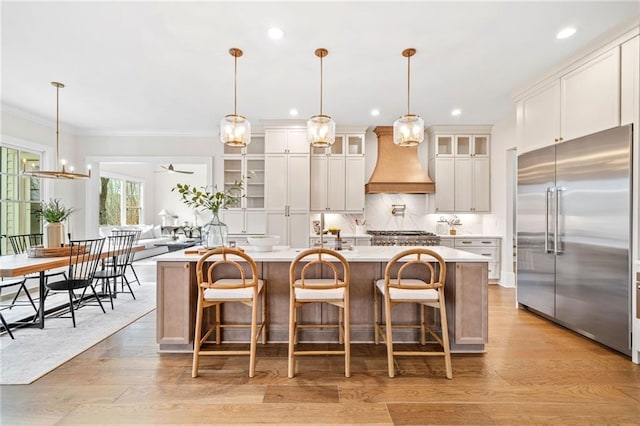 kitchen featuring crown molding, light countertops, a large island, stainless steel built in fridge, and custom range hood