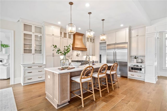 kitchen featuring light wood finished floors, tasteful backsplash, recessed lighting, custom range hood, and appliances with stainless steel finishes